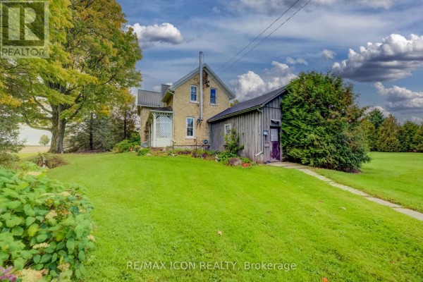 Side view of the farmhouse with a detached wooden shed and a large green lawn. - 9562 Wellington Rd 16 Road, Wellington North