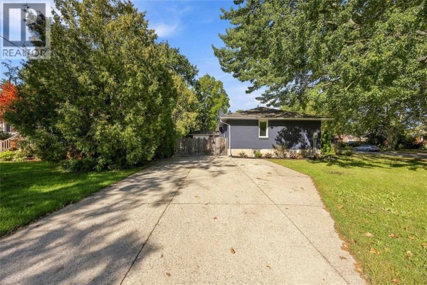 Concrete driveway leading to the side of a grey house with a wooden fence. - 957 Kensington Boulevard, Sarnia