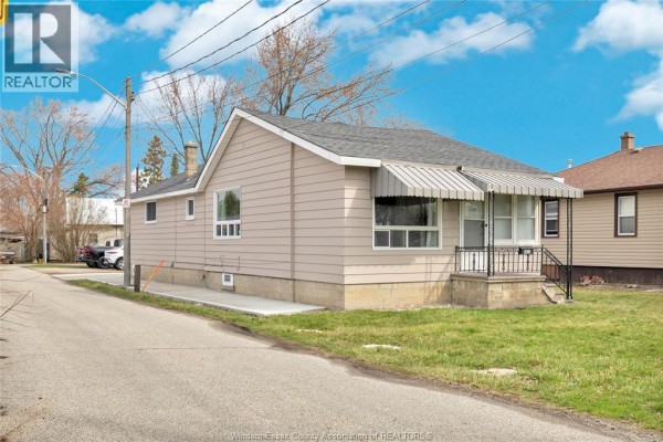 Side view of a beige house with a gray roof, concrete foundation and lawn. - 9572 Tecumseh Road, Windsor