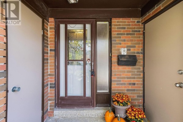 Close-up of a townhouse front door with sidelight, brick exterior, and decorative pumpkins and mums. - 41 Carl Shepway, Toronto