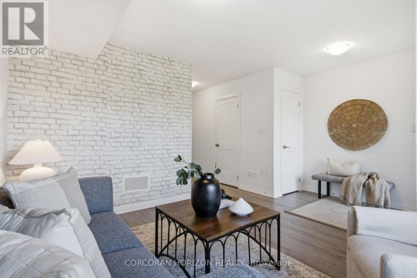 Living room with grey sofa, coffee table, and white painted brick accent wall. - 96 - 51 Sparrow Avenue, Cambridge