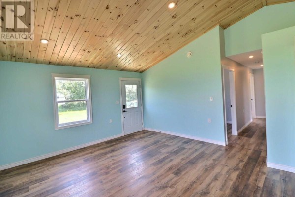 Living room with light blue walls, wood vaulted ceiling, and a door leading to a hallway. - 96 Arr Beach Lane, Beach Point