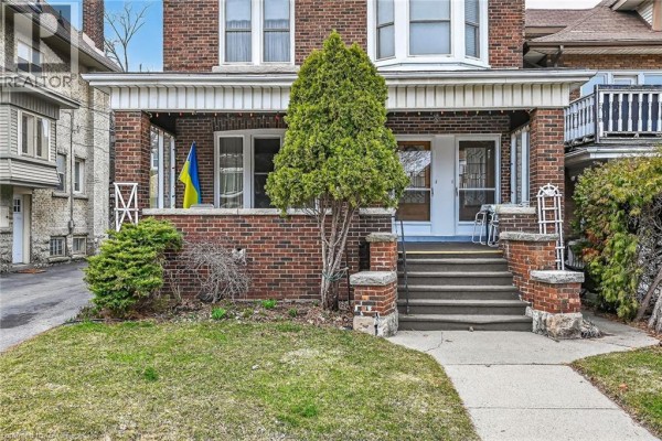 Close-up of the front porch entrance with steps, brick columns, and a Ukrainian flag. - 96 Barnesdale Boulevard, Hamilton