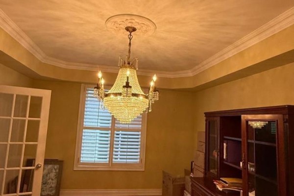 A formal dining room with a crystal chandelier, tray ceiling, large window with shutters, and a wooden cabinet. - 96 Bradgate Drive, Markham