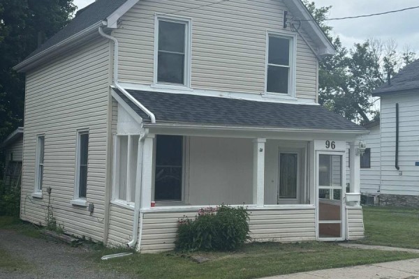 Side view of a two-story house with beige siding, white trim, and a covered front porch. - 96 Brock Street, Brockville