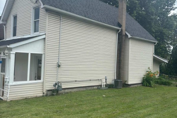 Side view of the house showing beige siding, a brick chimney, air conditioning unit, and green lawn. - 96 Brock Street, Brockville