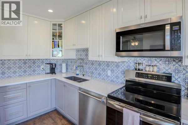 White and grey kitchen cabinets with a patterned tile backsplash and stainless steel appliances. - 96 Coachway Gardens Sw, Calgary