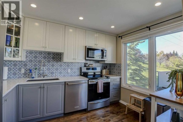 Corner kitchen with white cabinets, grey base cabinets, and a large window overlooking greenery. - 96 Coachway Gardens Sw, Calgary