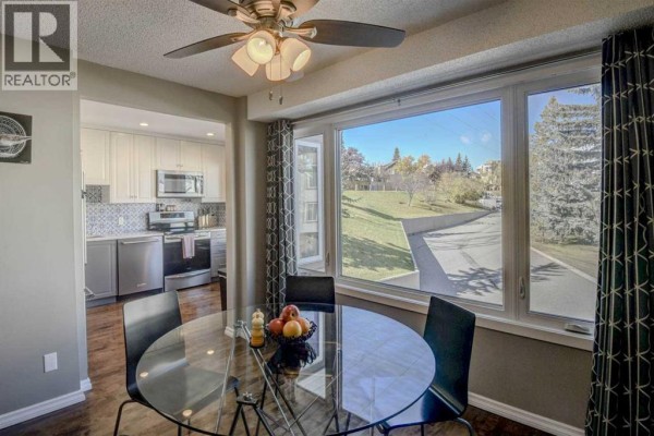 Round dining table with black chairs near a large bay window with a view of trees and grass. - 96 Coachway Gardens Sw, Calgary