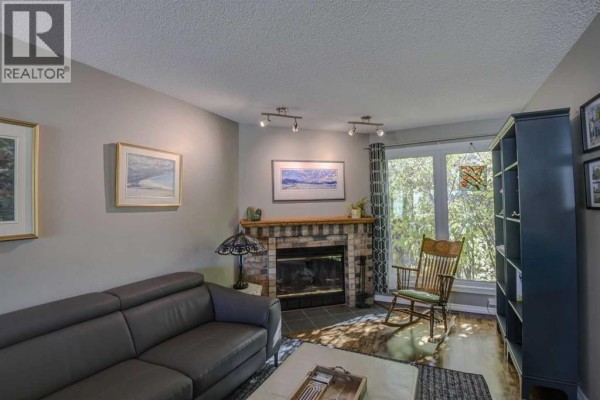 Living room with a grey sofa, brick fireplace, rocking chair, and a large bookcase. - 96 Coachway Gardens Sw, Calgary
