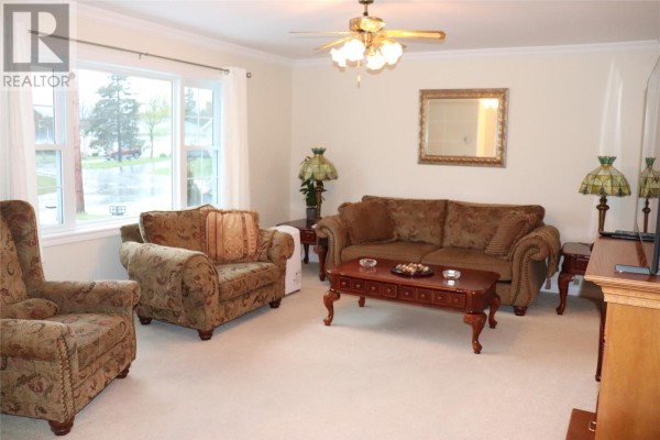 Living room with beige carpet, a bay window, sofa, armchairs, coffee table, and decorative lamps. - 96 Colonial Avenue, Stephenville