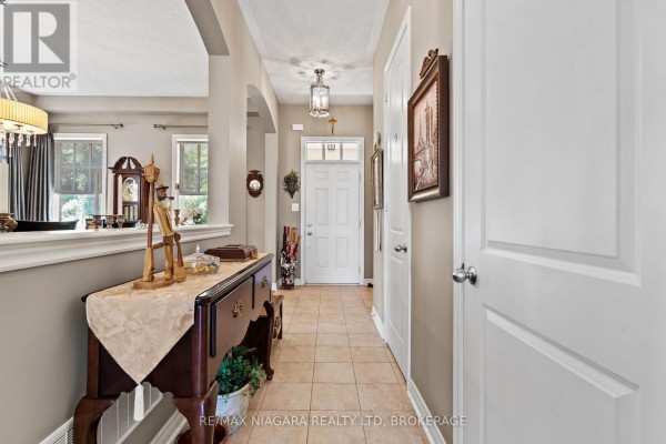 Tiled hallway with a console table, leading to a white front door and interior doors. - 96 Garrison Village Drive, Niagara On The Lake