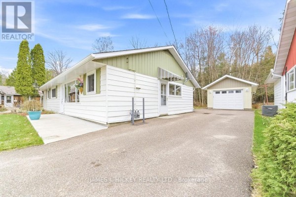 Side view of the white bungalow with green trim, showing the driveway and a detached garage. - 96 Glendale Avenue, Deep River