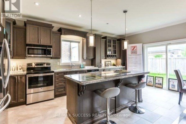 Kitchen with dark wood cabinets, granite countertops, stainless steel appliances, and island with stools. - 96 Nashville Circle, Hamilton