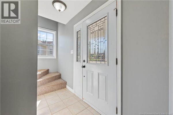 Interior view of the foyer with a tiled floor, beige carpeted stairs, and a white double door. - 96 Nicolas Street, Dieppe