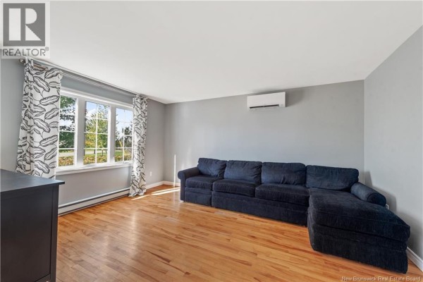 Living room with light grey walls, hardwood floors, a large navy sectional sofa, and a bay window. - 96 Nicolas Street, Dieppe