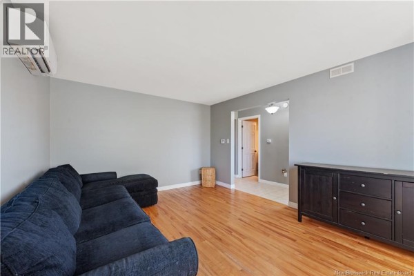 Living room with grey walls, hardwood floors, a navy sectional sofa, a black dresser, and an entrance to another room. - 96 Nicolas Street, Dieppe
