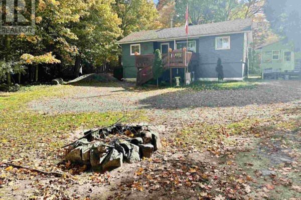View of the house from the yard, with a stone fire pit in the foreground. - 96 Olar Side Rd, Goulais River