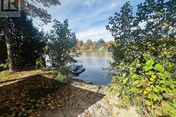 Waterfront view with trees, a jet ski in the water, and a sandy shore. - 96 Olar Side Rd, Goulais River