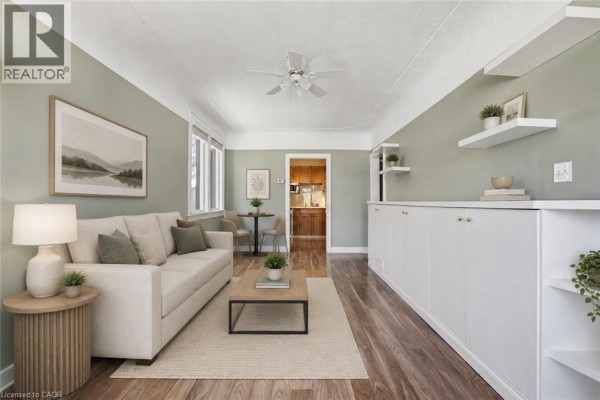 Living room with a beige sofa, coffee table, rug, green walls, built-in white cabinetry, and a view of the kitchen. - 96 Paling Avenue, Hamilton