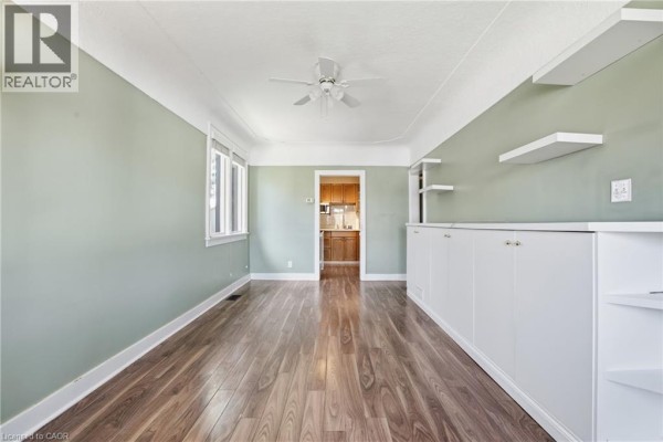 Living room with a beige sofa, coffee table, rug, green walls, built-in white cabinetry, and a view of the kitchen. - 96 Paling Avenue, Hamilton