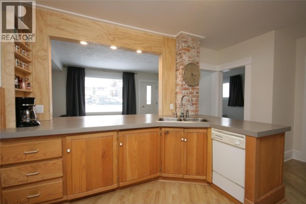 Kitchen interior with wooden cabinets, a stainless steel sink, and a brick accent wall. - 960 Nicola Street, Kamloops