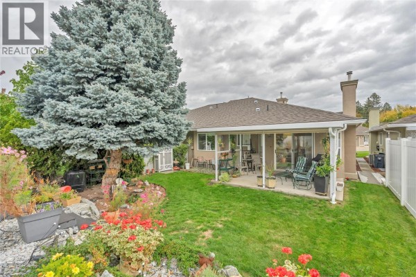 Backyard patio area with green grass, large tree, and colourful flowers. - 9600 Turner Street Unit# 20, Summerland