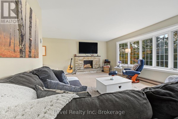 Living room with a stone fireplace, mounted television, large sectional sofa, and bay window with trees outside. - 9614 Hwy 63, Unorganized Townships