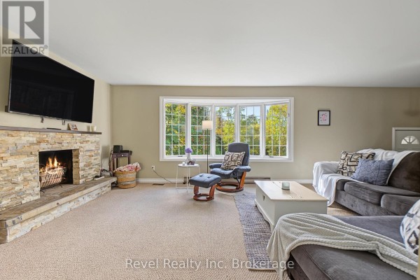 Living room with plush carpet, a stone fireplace, a large bay window overlooking trees, and comfortable seating. - 9614 Hwy 63, Unorganized Townships