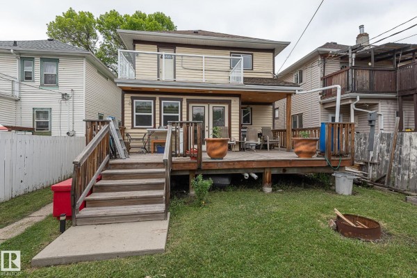 Rear view of a two-story yellow house with a large wooden deck and stairs. - 9623 110a Av Nw, Edmonton
