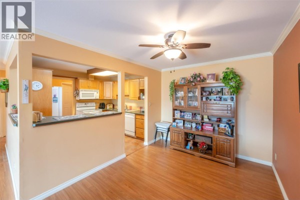 Living room with a beige sofa, armchair, gas fireplace, and large sliding glass doors. - 965 King Street Unit# 203, Penticton