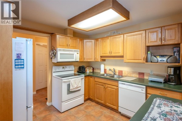 Living room with a beige sofa, armchair, gas fireplace, and large sliding glass doors opening to a sunroom. - 965 King Street Unit# 203, Penticton