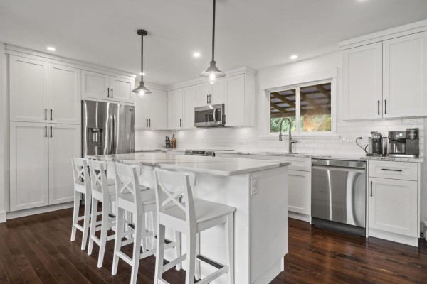 Modern white kitchen with a large island, stainless steel appliances, and dark wood floors. - 9650 Aberdeen Crescent, Rosedale, Rosedale