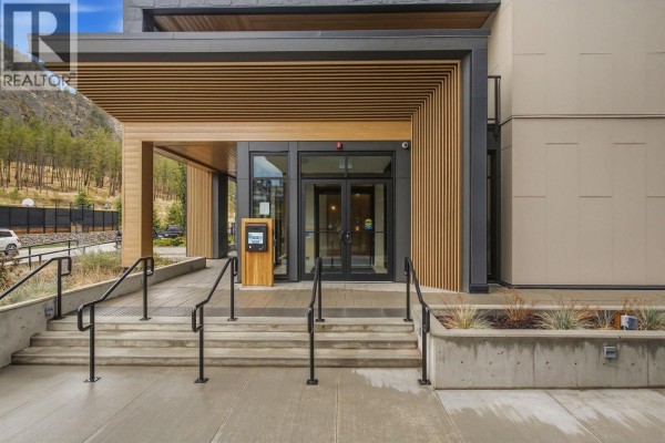 Modern building entrance with glass doors, wood paneling, and concrete stairs. - 9652 Benchland Drive Unit# 404, Lake Country