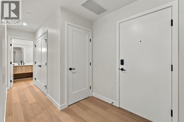Apartment hallway with light wood floors and white doors leading to rooms. - 9652 Benchland Drive Unit# 404, Lake Country