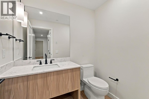Powder room with a white vanity, marble countertop, and black fixtures. - 9652 Benchland Drive Unit# 404, Lake Country