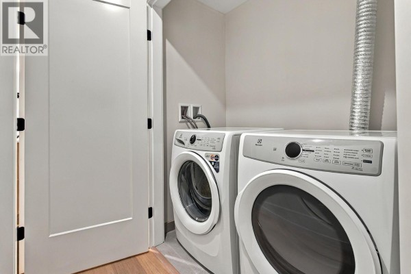 Laundry room with a stacked white washer and dryer in a small space. - 9652 Benchland Drive Unit# 404, Lake Country