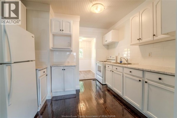White kitchen with white cabinetry, granite countertops, stainless steel appliances, and dark hardwood floors. - 966 Curry Avenue, Windsor