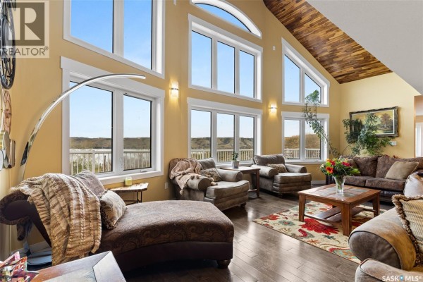 Living room with large windows and vaulted wood ceiling, view of open-concept kitchen. - 966 Tatanka Drive, Buffalo Pound Lake