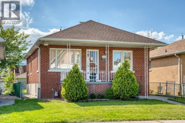 Red brick bungalow with a white porch railing and two green bushes. - 969 Langlois, Windsor
