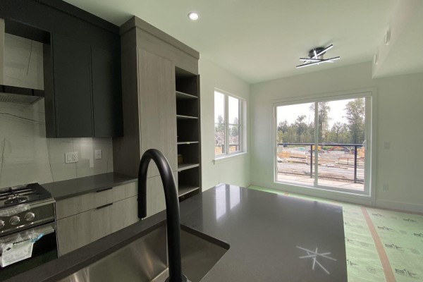 Kitchen island with sink, dark grey and wood cabinets, stainless steel gas range, and sliding doors with a view. - 97 7895 162 Street, Surrey