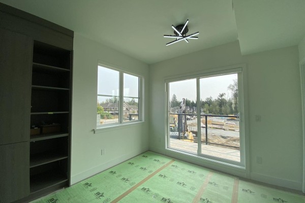 Bright room with two windows, sliding doors, a dark wood bookshelf, and a view of surrounding houses and construction. - 97 7895 162 Street, Surrey