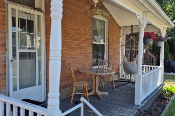 Close-up of a covered porch with a small table, chairs, and a hanging hammock. - 97 Colborne Street S, Simcoe
