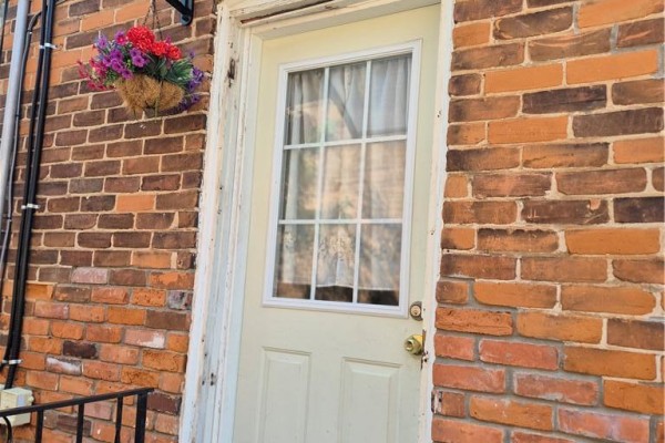 Close-up of a cream-colored door with a glass pane, surrounded by red brick. - 97 Colborne Street S, Simcoe
