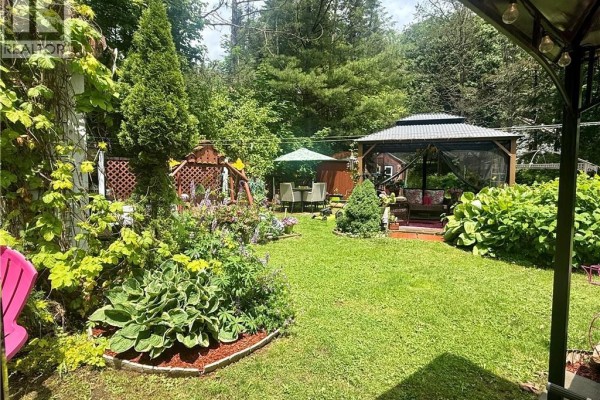 View of a backyard with a gazebo, shed, patio furniture, and vibrant green plants and flowers. - 97 Main Street, St George
