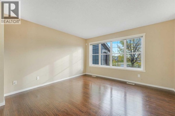 Empty living room with dark wood floors, beige walls, and large window. - 97 Marine Drive Se, Calgary