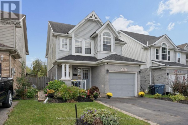 Side view of the two-story grey house with a driveway, garage, and front lawn with flowers. - 97 Teal Drive, Guelph
