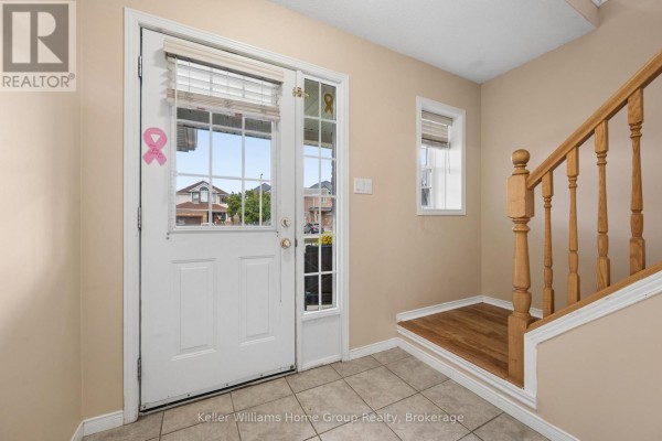 Interior view of a house entryway with a white front door, glass sidelights, tiled floor, and wooden staircase. - 97 Teal Drive, Guelph
