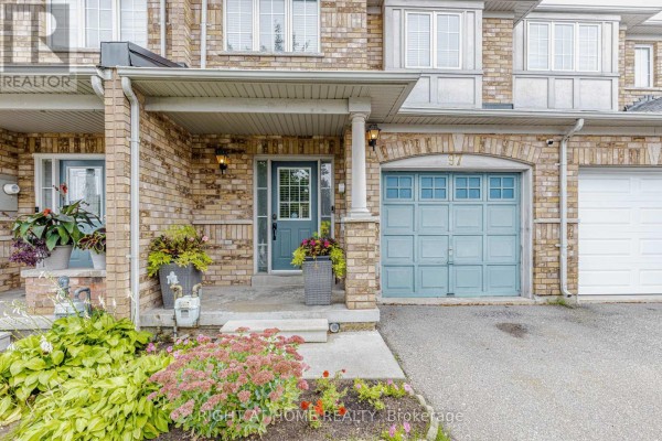 Close-up of townhouse entrance with covered porch, brick facade, and blue garage door. - 97 Timbertop Crescent, Brampton