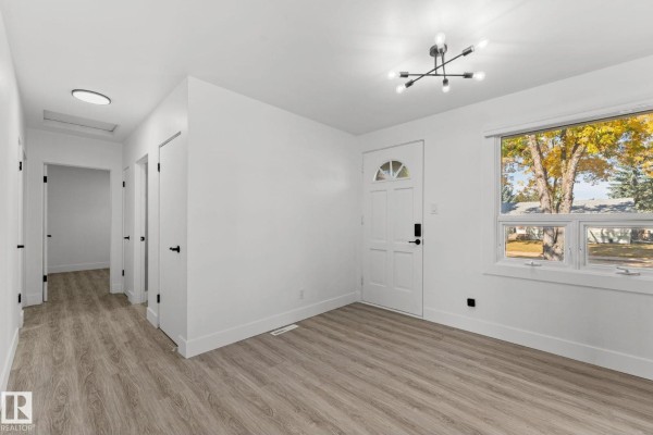 Interior view of a hallway with a white front door and a window overlooking autumn trees. - 970 Alder Ave, Sherwood Park
